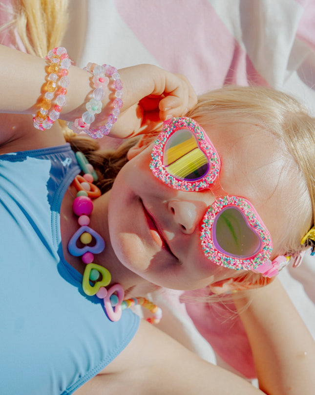 lifestyle image of child laying on beach towel wearing sprinkle heart kid's swim goggles 