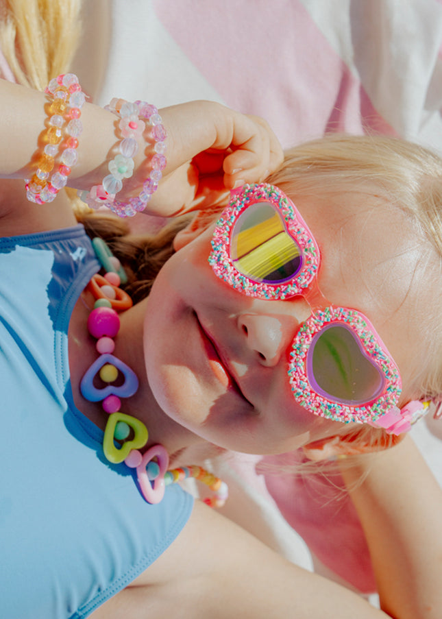 lifestyle image of child laying on beach towel wearing sprinkle heart kid's swim goggles 