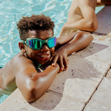 kid hanging out pool side wearing streamline swim goggles in current green showing the textured silicone frame