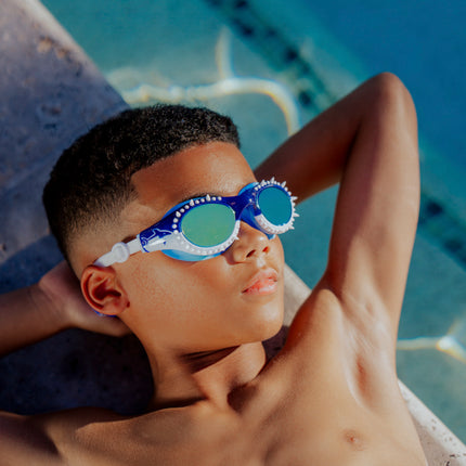 boy laying next to pool relaxing wearing shark surge kids swim goggles in great white strike showing silicone spike detail and shark printed frame