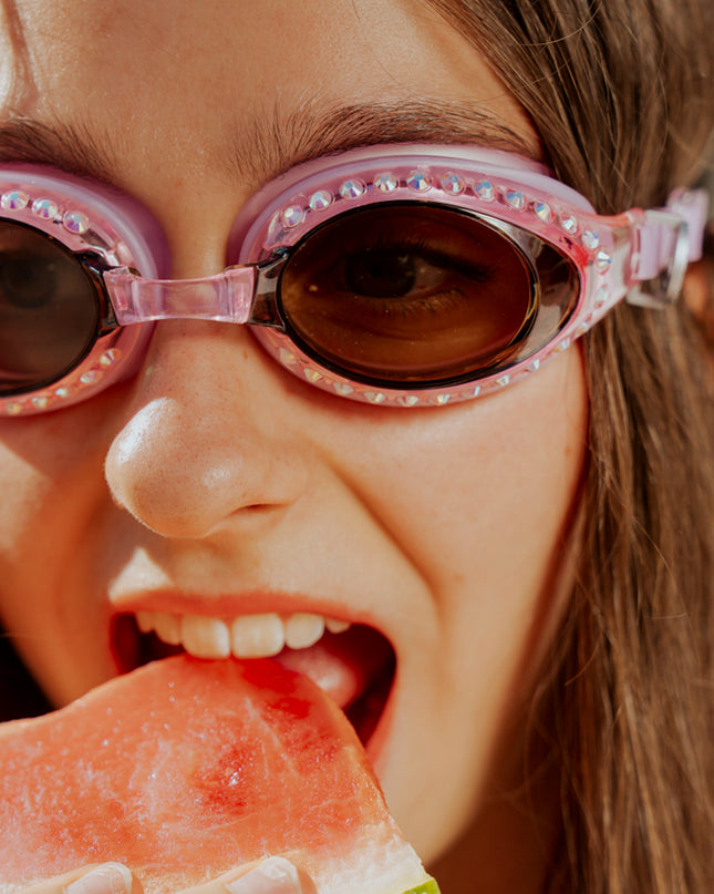 teen girl eating watermelon poolside wearing seek tranquility swim goggles in peaceful pink showing a dusty pink swim goggle with rhinestones