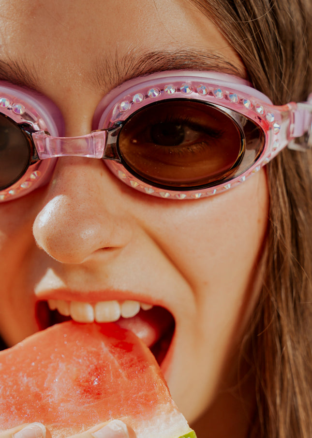 teen girl eating watermelon poolside wearing seek tranquility swim goggles in peaceful pink showing a dusty pink swim goggle with rhinestones