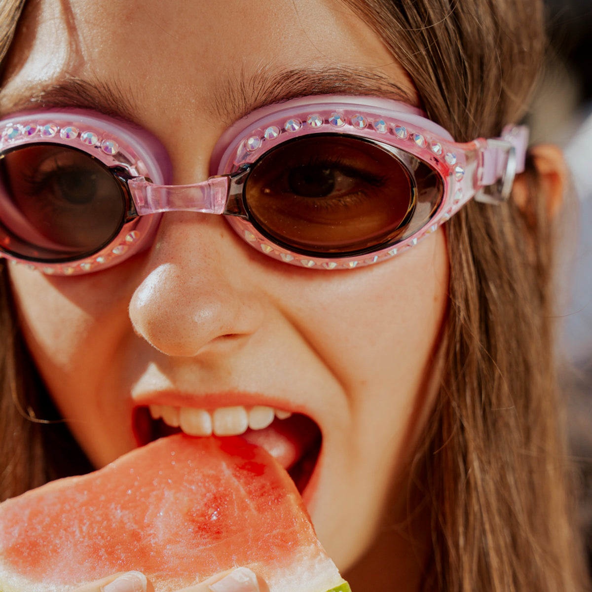 teen girl eating watermelon poolside wearing seek tranquility swim goggles in peaceful pink showing a dusty pink swim goggle with rhinestones