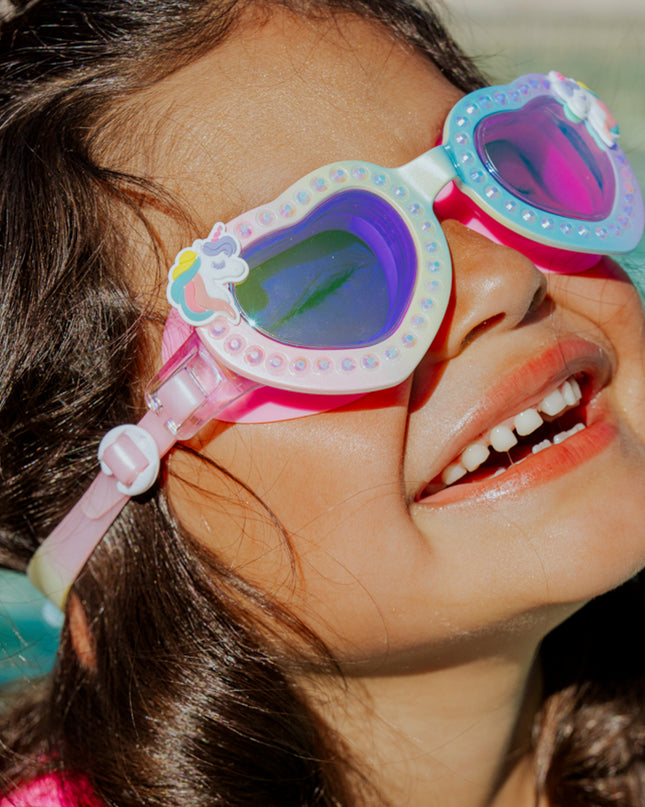 girl smiling and laughing wearing uniglow kids heart shaped swim goggles showing a pastel rainbow coloring, rhinestones and unicorn detail