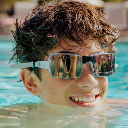 teen boy swimming and smiling while wearing velocity swim goggles in onyx showing frameless black lens and tan silicone strap