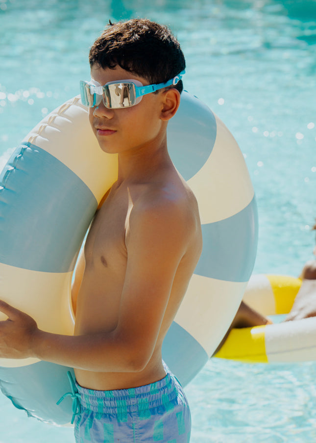 junior boy standing poolside wearing velocity swim goggles in wave blue showing frameless lens and blue silicone strap