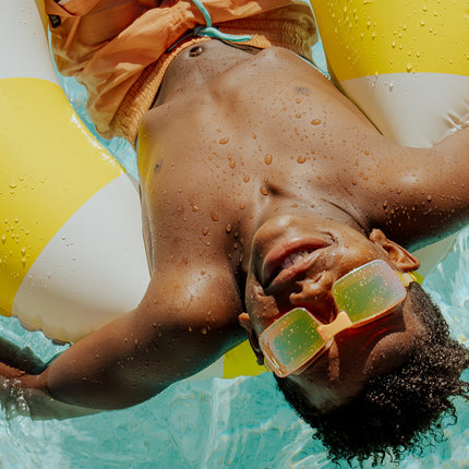 boy swimming relaxing in inner tube wearing velocity swim goggles in volt showing gold colored frameless lens