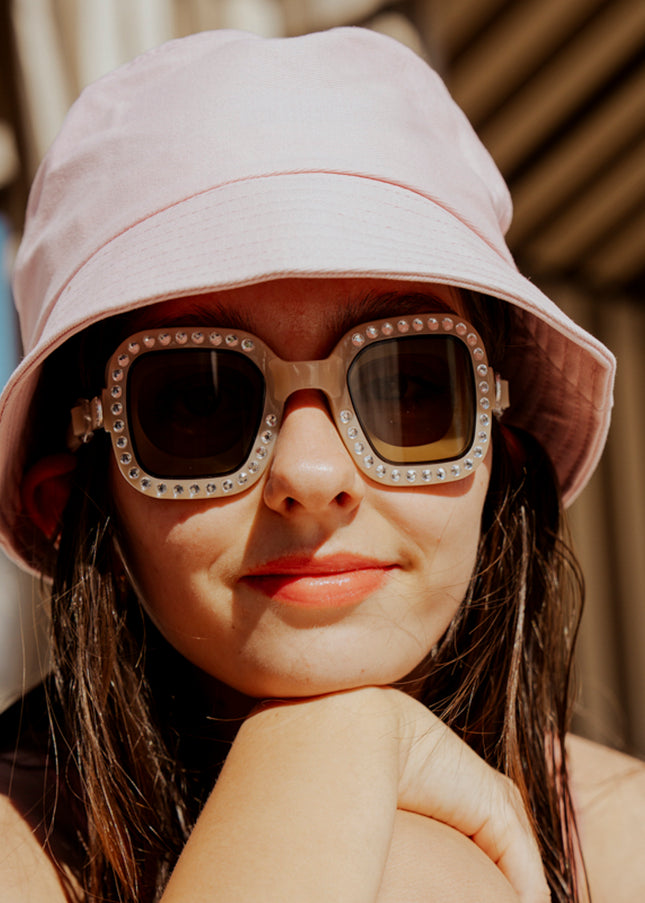 teen girl sitting poolside wearing bring vibrancy swim goggles in opal showing wide square framed swim goggles with rhinestones and tinted lens
