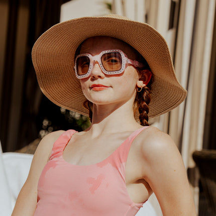 teen girl sitting poolside wearing vibrancy swim goggles in rose quartz showing a pale pink large square frame, rhinestones and tined lens