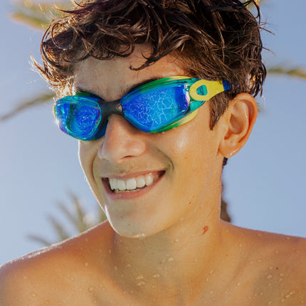 teen boy wearing sitting poolside wearing voyage swim goggles in ever green showing reflective lens, and silicone frame