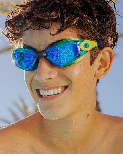 teen boy wearing sitting poolside wearing voyage swim goggles in ever green showing reflective lens, and silicone frame