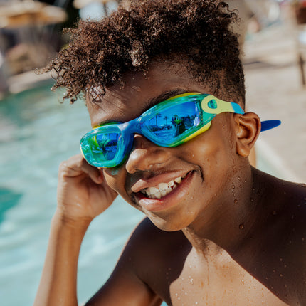 boy sitting poolside smiling wearing voyage swim goggles in rainforest showing reflective lens and silicone frame