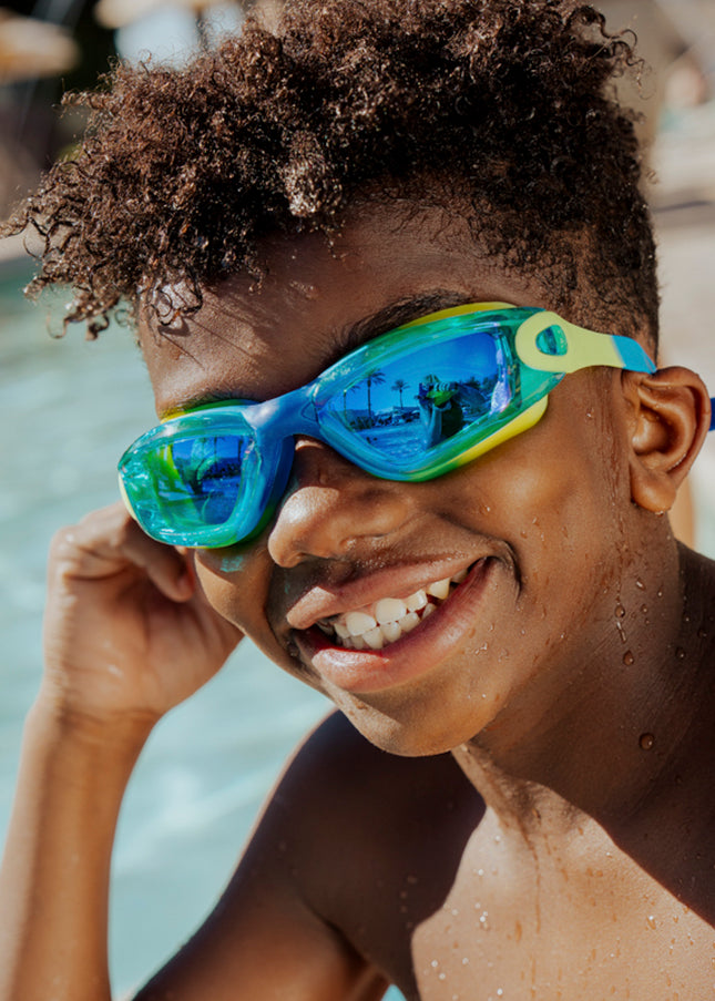 boy sitting poolside smiling wearing voyage swim goggles in rainforest showing reflective lens and silicone frame